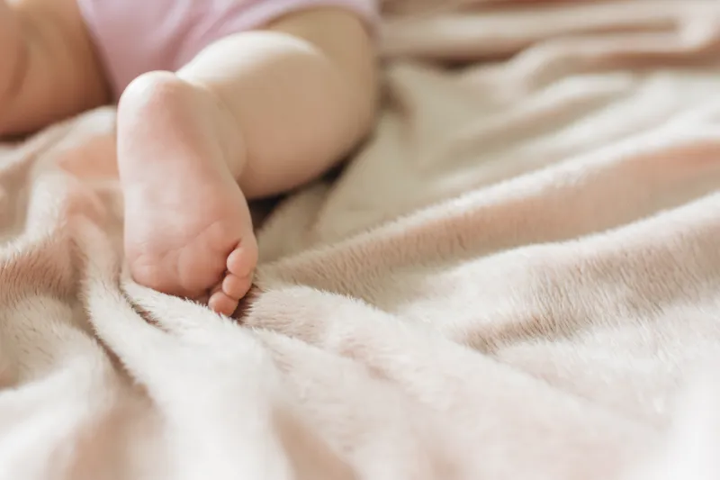 Ein kleiner, nackter Babyfuß liegt weich gebettet auf einer kuscheligen, hellrosa Decke – passend zum Gedicht "Vatergedanken"